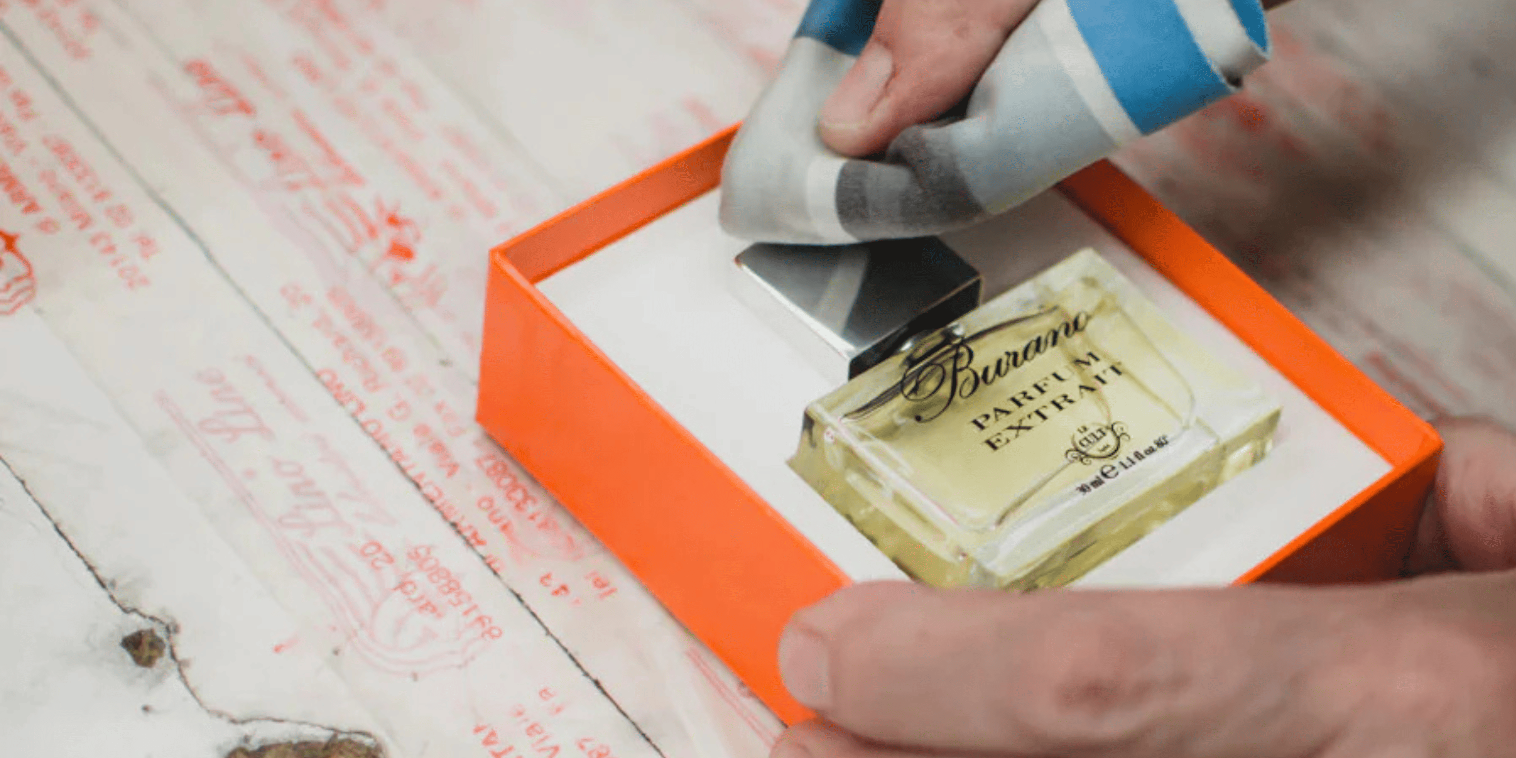 una mano pulisce con un panno una confezione del profumo Burano di Le Cult: mettiamo cura in ogni dettaglio